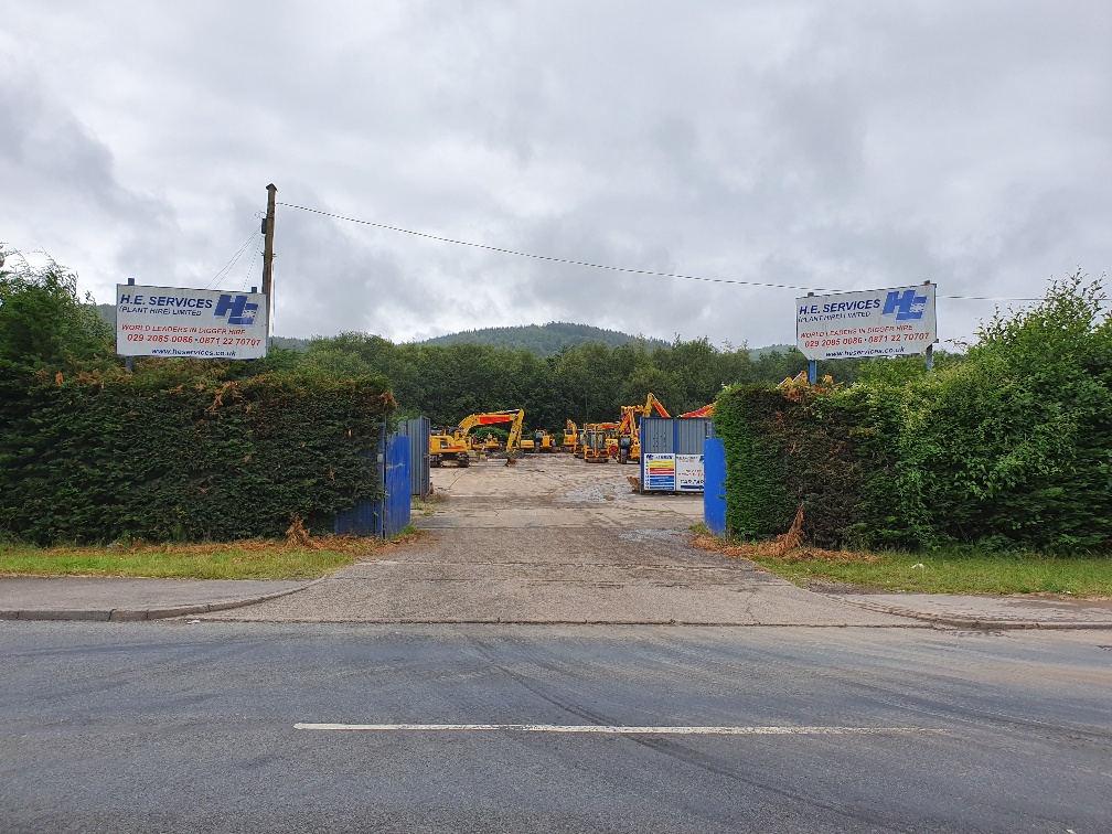 Cardiff Plant hire Depot - H. E. services plant hire - Plant hire in Cardiff - Entrance to depot with a sign either side of the entrance and the middle shows the yard with excavators in